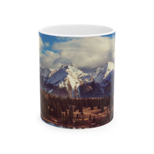 The scenic mountain landscape with snow-capped peaks, evergreen trees, and a cloudy blue sky.